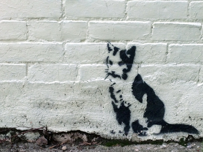 Stencil of a cat on a brick wall.